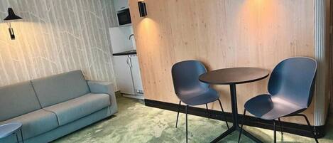 A room with a sofa, two chairs, a small table, a wooden partition, and a kitchen area.