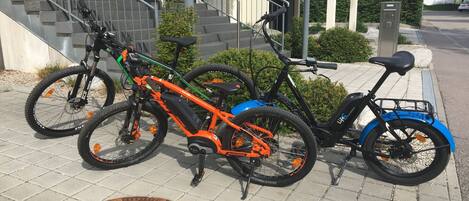 Una bicicleta estacionada en un área pavimentada, con una tapa de registro, un edificio con escaleras y un cartel al fondo.