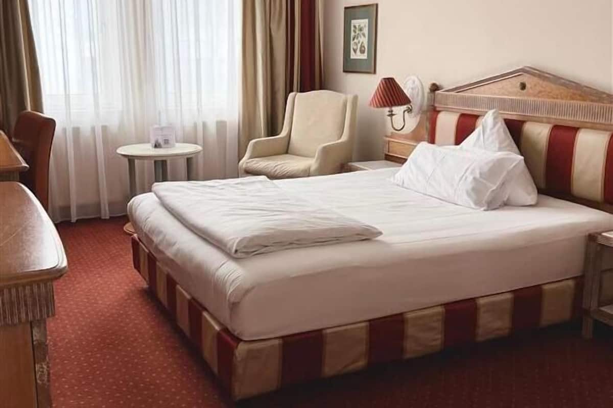 Una habitación de hotel con una cama grande, una silla, una mesita y una lámpara.
