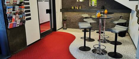 Un interior moderno con pasillo cubierto de alfombra roja, una escalera, una zona de bar con taburetes y una exhibición de folletos en la pared.