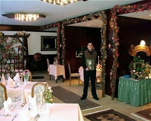 Un comedor con mesas dispuestas para una comida, una persona de pie cerca de la entrada y un centro de mesa decorativo sobre una mesa.