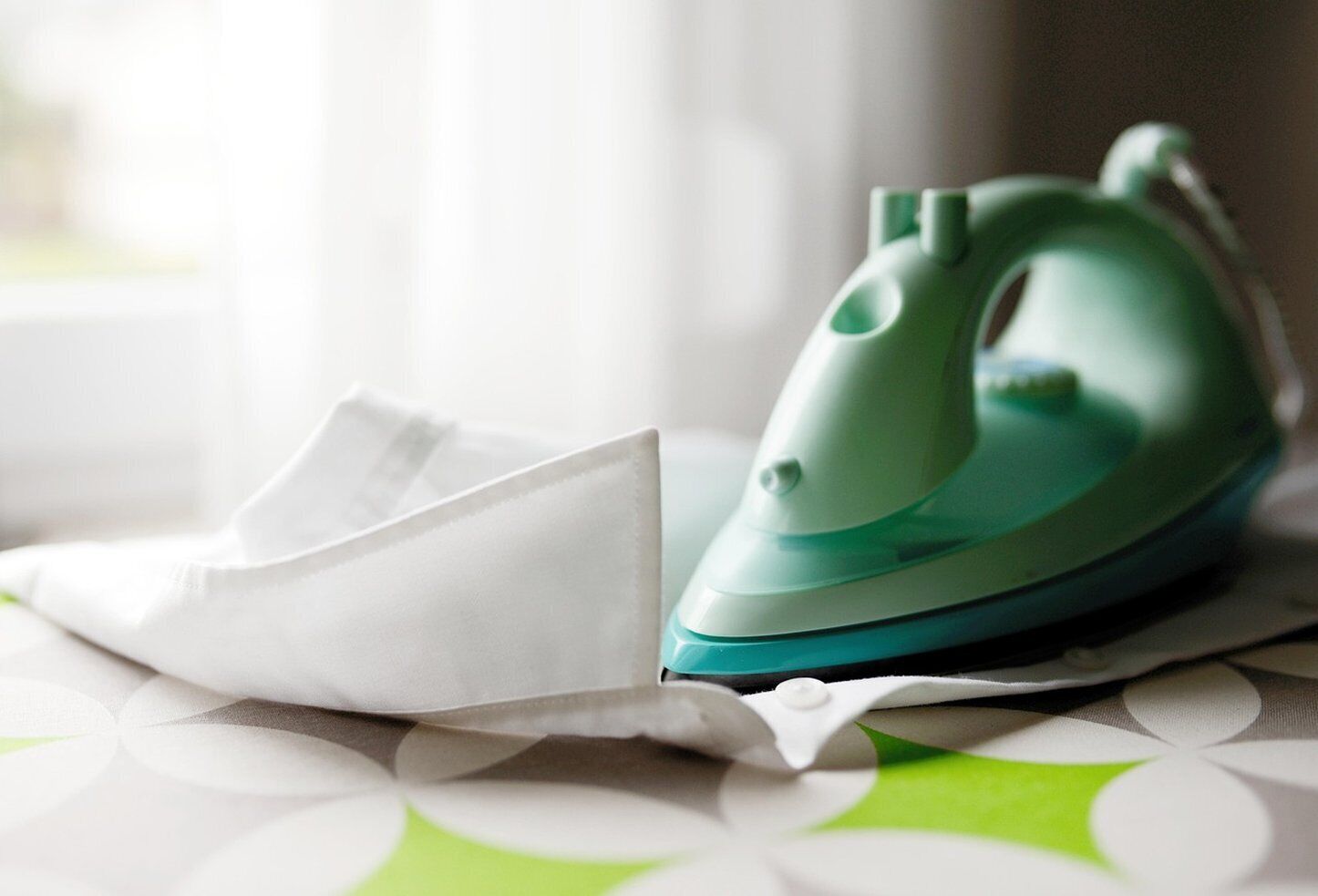 A green iron on a table with a white cloth.