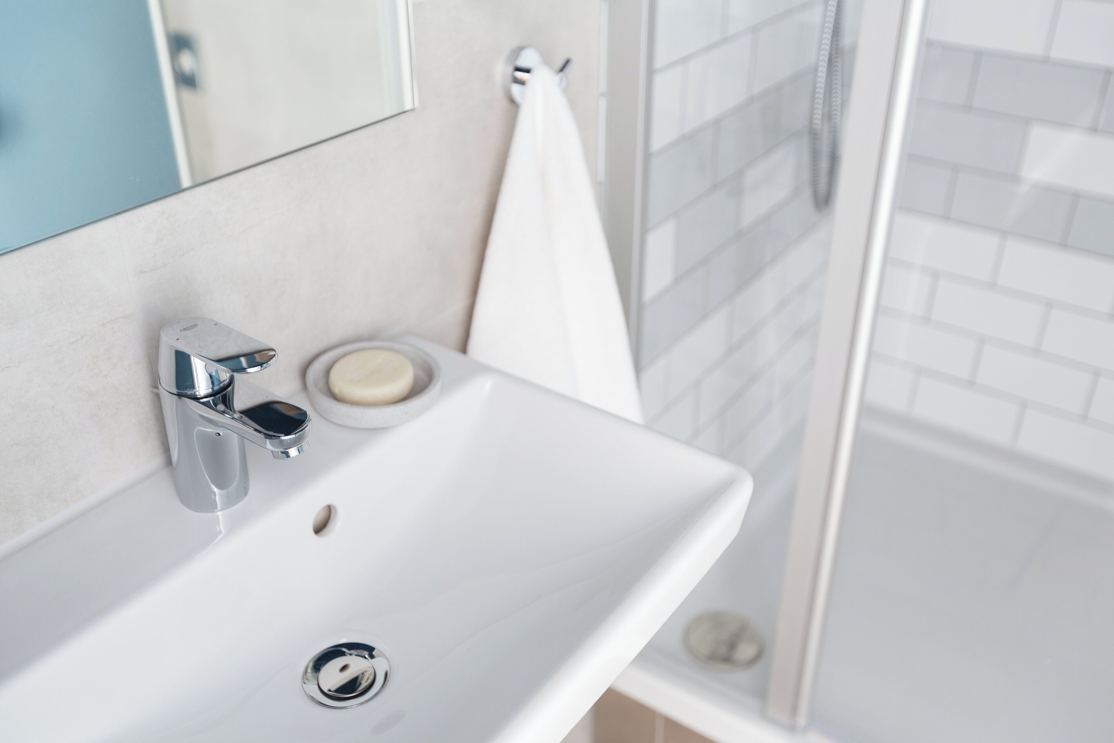 A modern bathroom with a white sink, chrome faucet, and a glass shower enclosure.