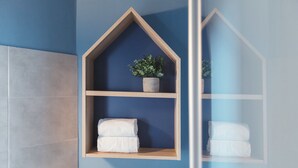 Un baño con pared azul, estantes de madera, una planta en maceta y toallas dobladas con cuidado.