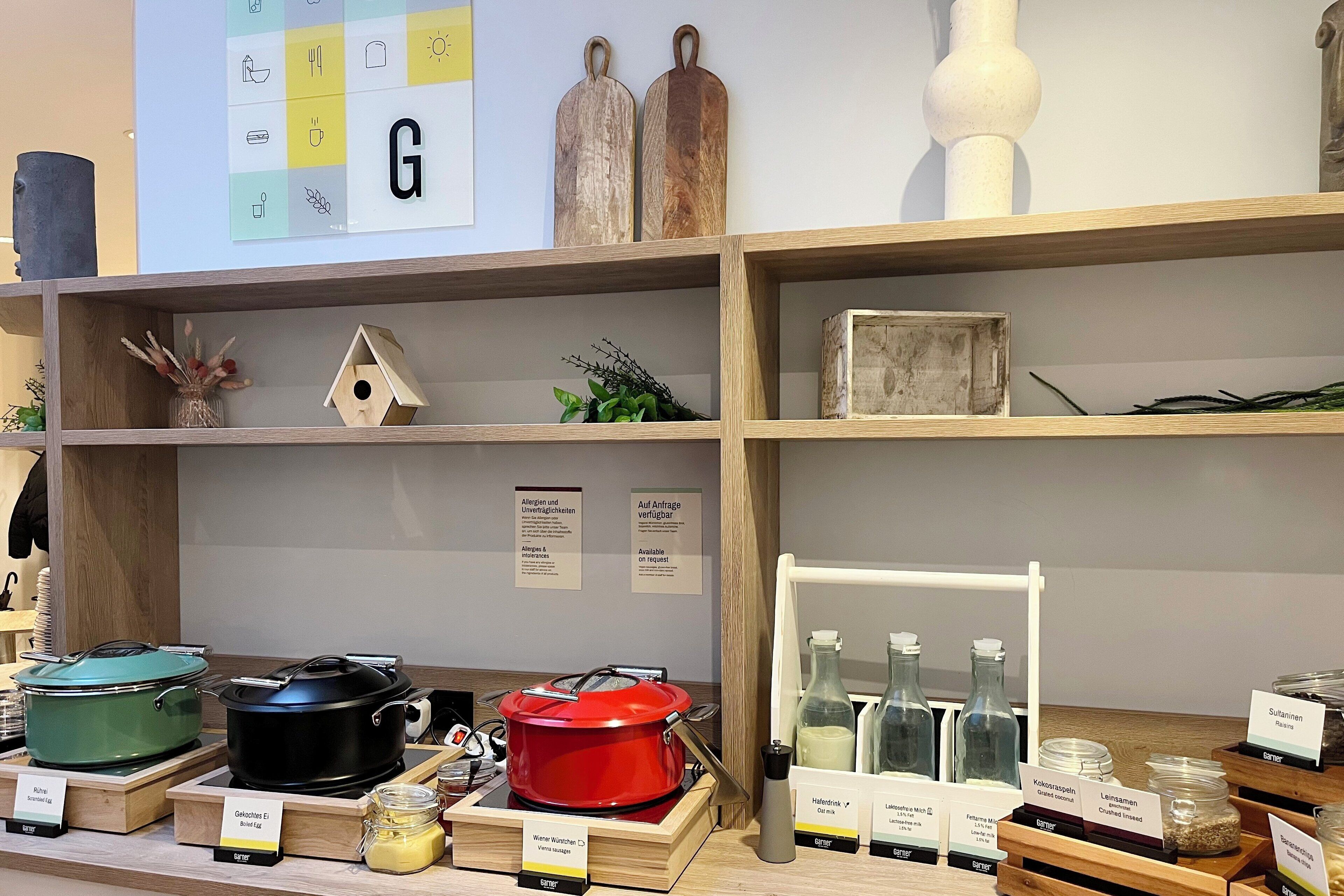 A kitchen display with various cooking pots, a red slow cooker, and labeled containers.
