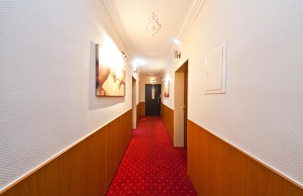Un couloir d’hôtel avec un tapis rouge, des boiseries et un lustre.