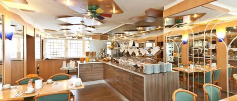 A modern restaurant with wooden flooring, green upholstered chairs, and a central island with food display.