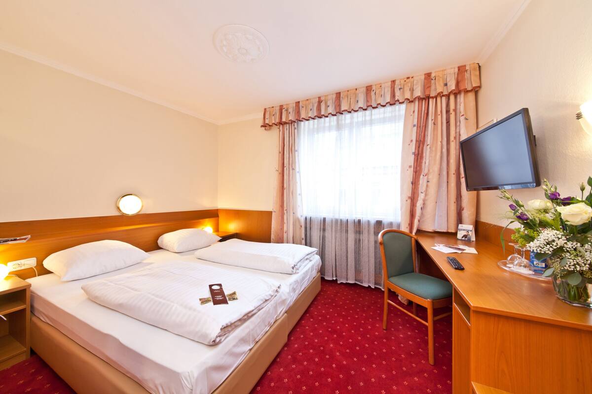 A hotel room with two beds, a desk with a chair, a television, and a window with curtains.