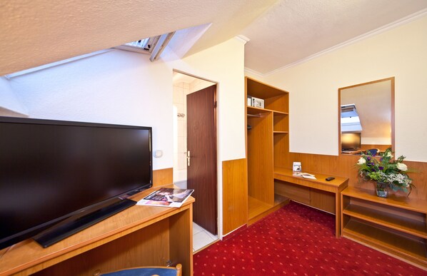 Habitación de hotel con televisión, escritorio de madera, alfombra roja, armario y espejo.