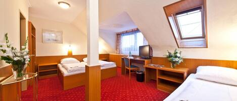 A hotel room with a red carpet, two beds, a desk, a TV, and a window.