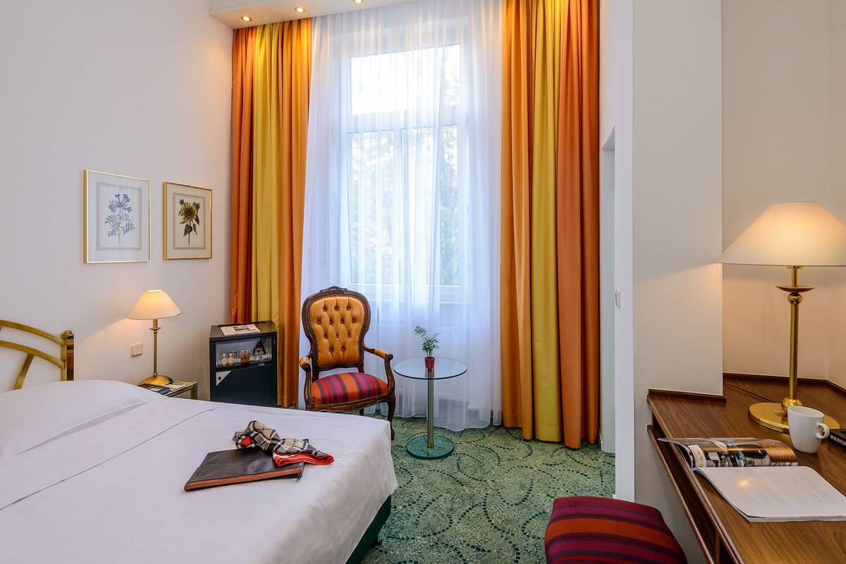 Ein Hotelzimmer mit einem Bett, einem Sessel, einem Schreibtisch, einer Lampe und einem fensterbepflanzten Fenster.