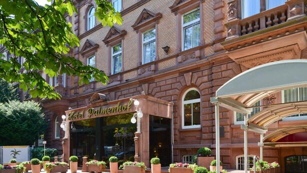 Ein historisches Gebäude mit einem beeindruckenden Eingangsbereich, großen Fenstern und einem gepflegten Garten mit Topfpflanzen.