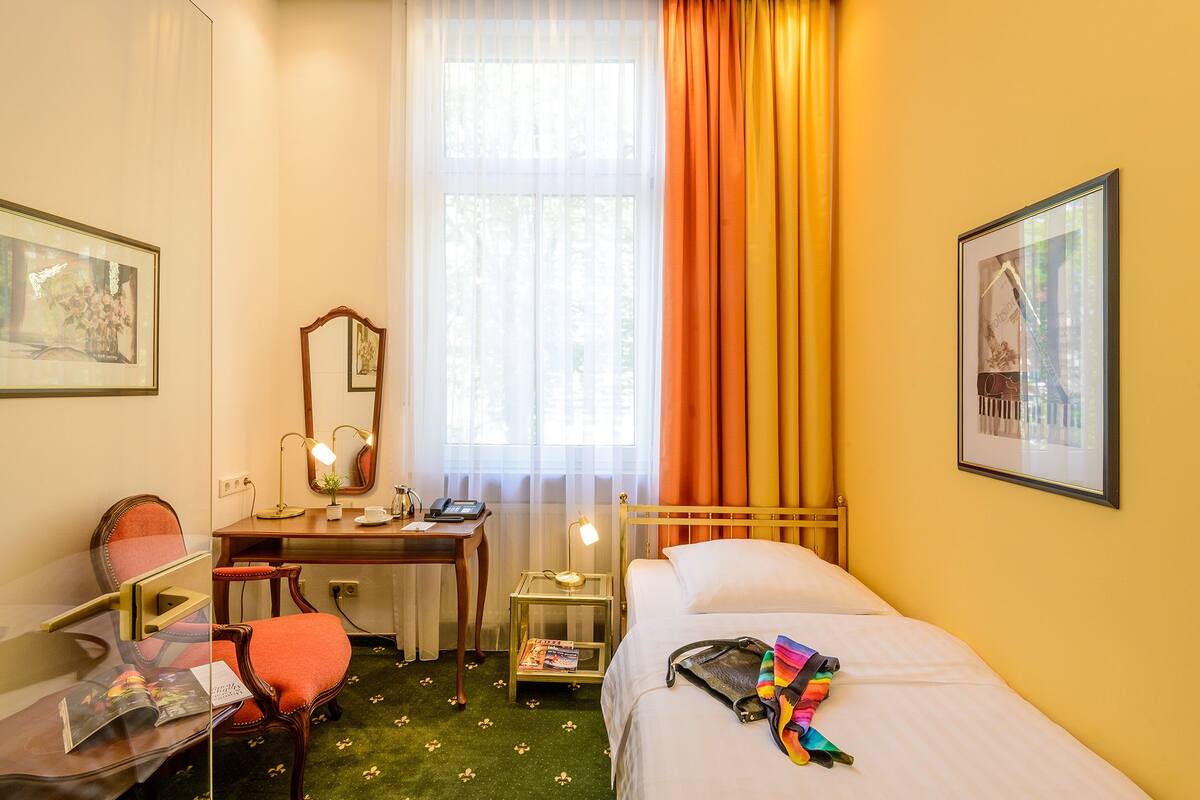 Ein Hotelzimmer mit Bett, Schreibtisch, Stuhl, Spiegel und einem Fenster mit Vorhängen.