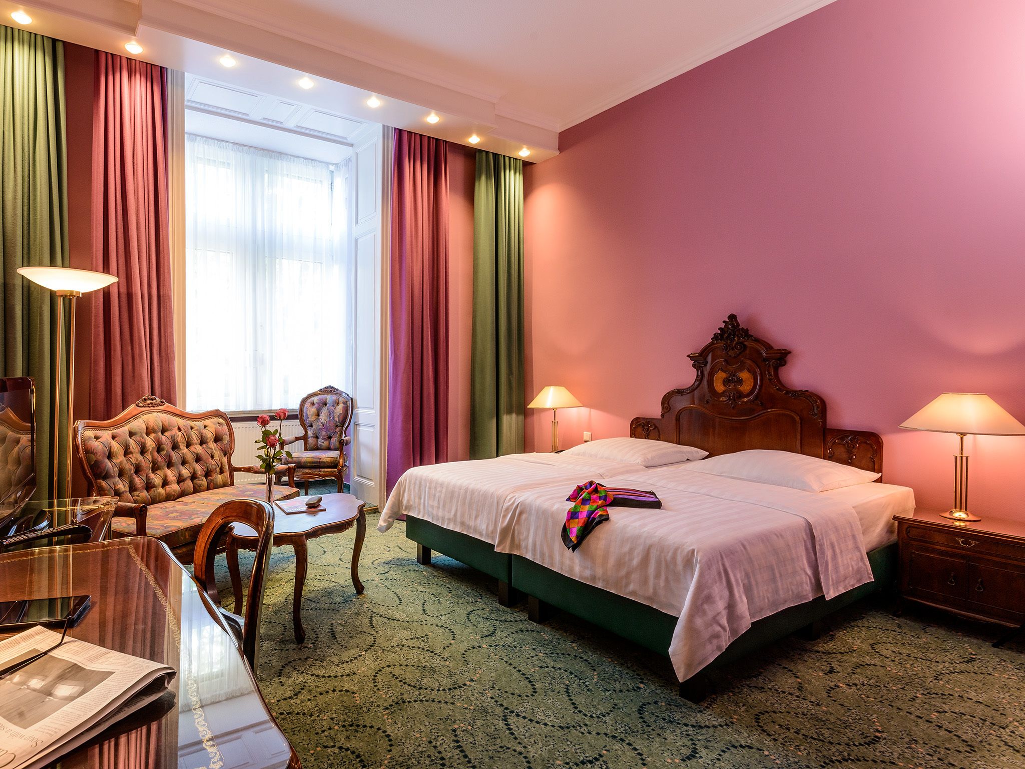 A hotel room with a bed, two bedside tables, a chair, a desk, and a window with curtains.