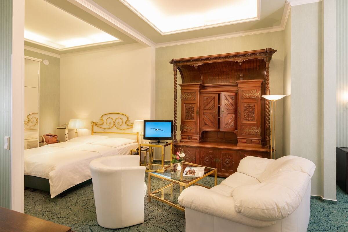 Ein Hotelzimmer mit zwei Betten, einem Fernseher, einem Holzschrank, einem Glastisch und einem weißen Sessel.