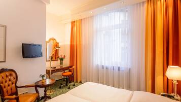 A hotel room with a bed, a desk with a chair, a television, a mirror, and a window with curtains.