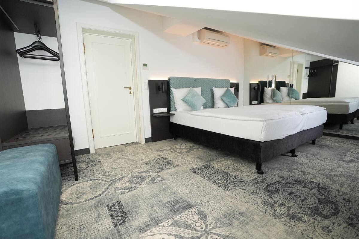 Ein modernes Hotelzimmer mit einem großen Bett, einem Nachttisch, einem Kleiderhaken und einem gemusterten Teppich.