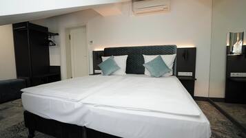 Un lit bien fait, avec du linge de lit blanc et deux coussins turquoise, une tête de lit noire et un climatiseur fixé au mur.