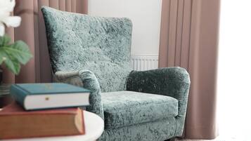 Un fauteuil confortable, revêtu d’un tissu texturé, placé à côté d’un radiateur et de rideaux.
