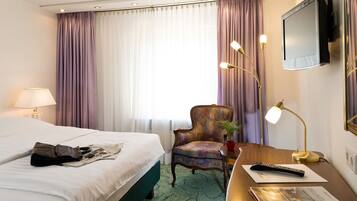 A hotel room with a bed, a desk with a lamp, a chair, and a television mounted on the wall.