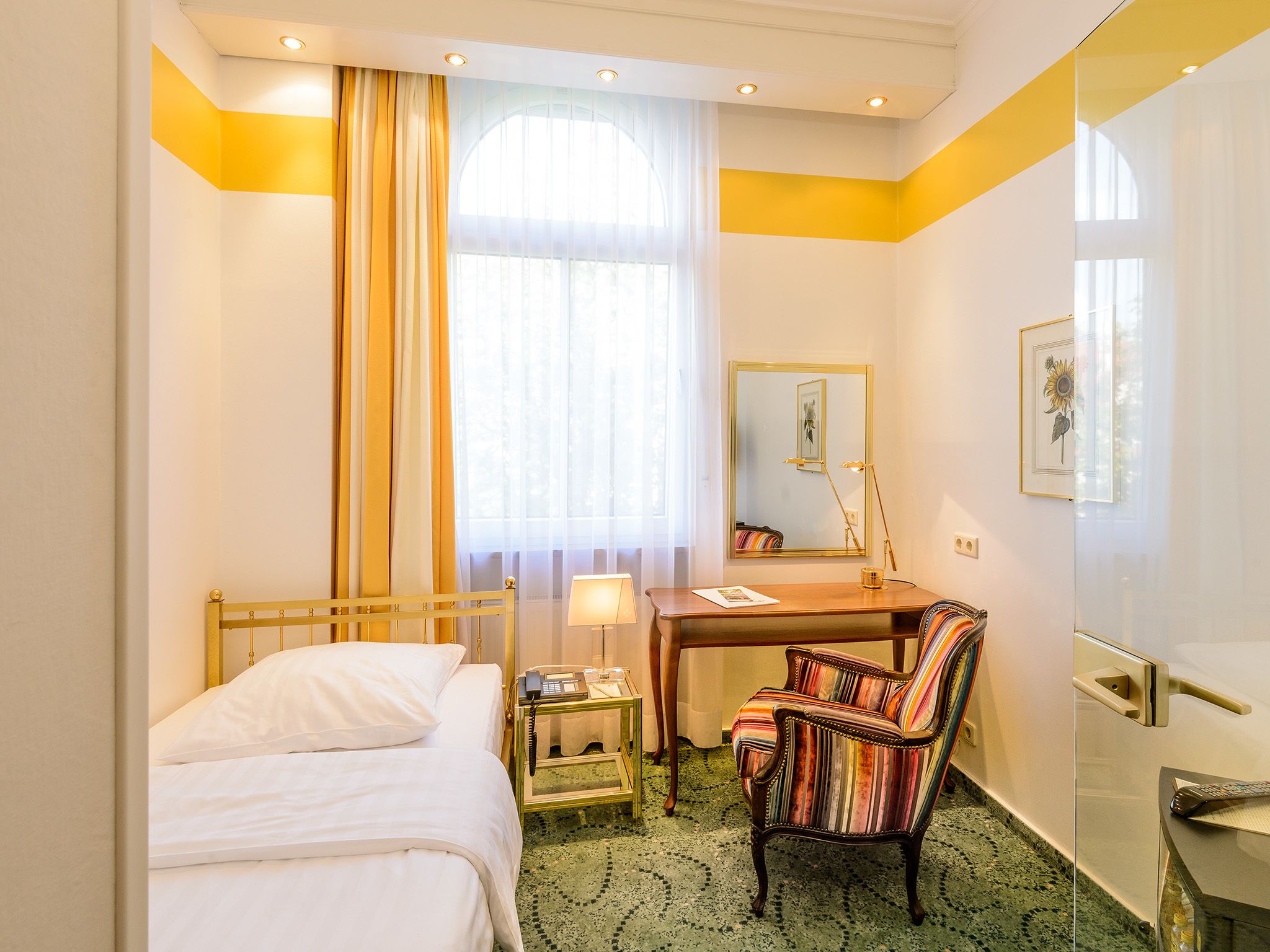 A hotel room with a bed, a desk, a chair, a mirror, and a window with curtains.