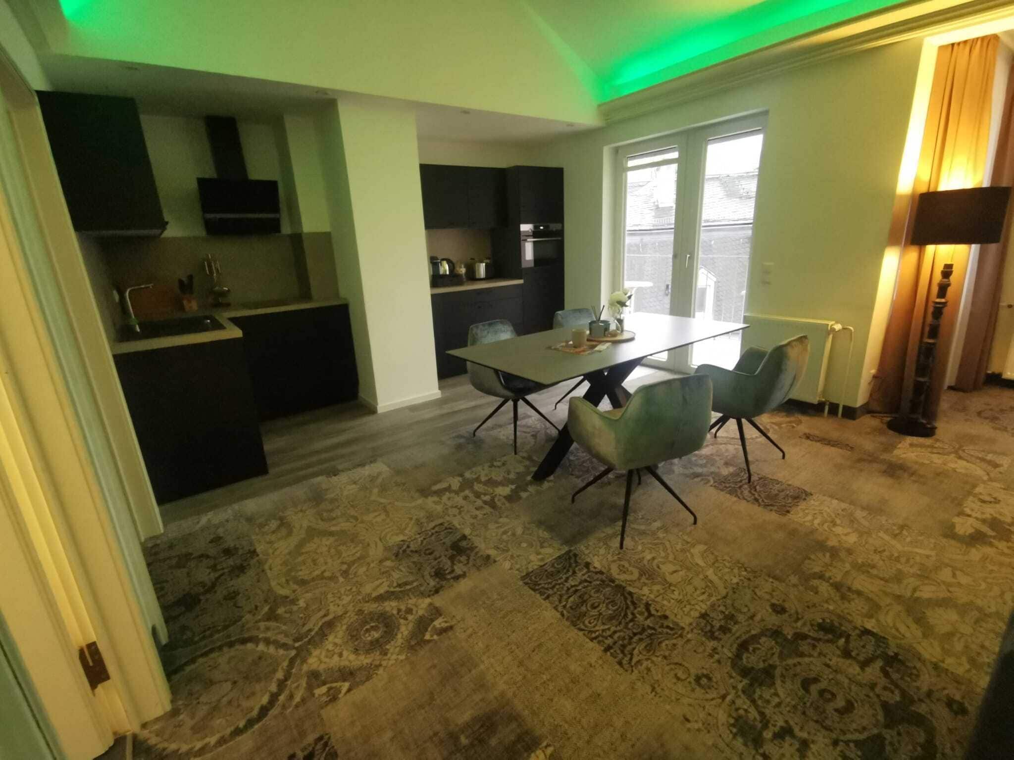A modern kitchen with dark cabinetry, a dining area with a table and chairs, and a patterned carpet.