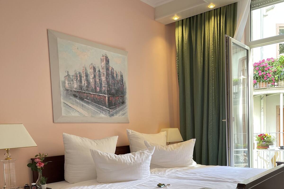 Ein Hotelzimmer mit einem großen Bett, einem Nachttisch mit Lampe, einem Bild an der Wand und Blick auf den Außenbalkon.