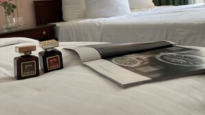 Ein ordentlich bezogenes Bett mit weißen Leinentüchern, zwei Flaschen i.puro ätherischer Öle und eine Zeitschrift auf dem Bett.