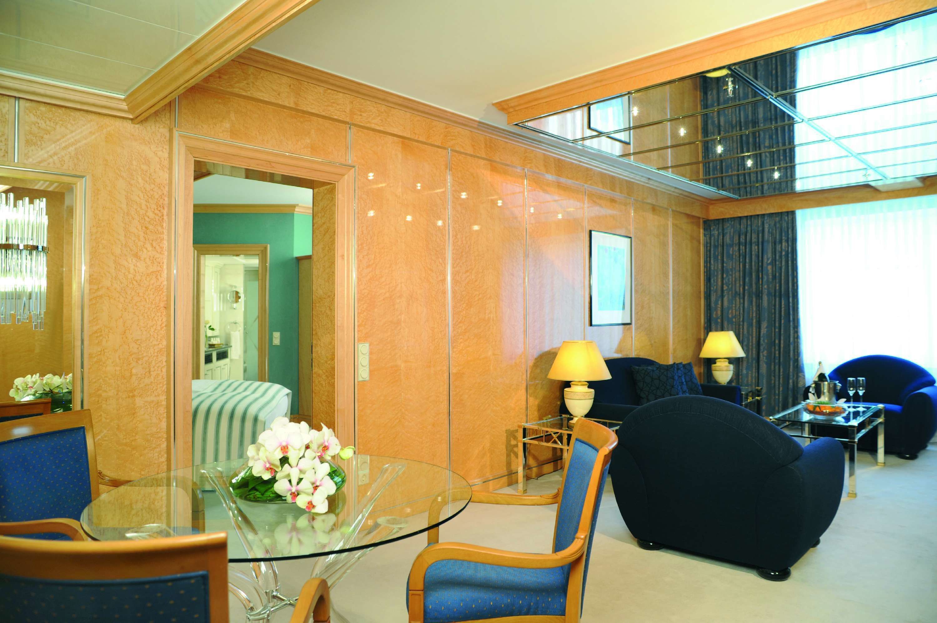 Een hotel lobby met een glazen tafel, blauwe stoelen, een bank en een lamp.