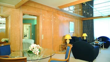 A hotel lobby with a glass table, blue chairs, a sofa, and a lamp.
