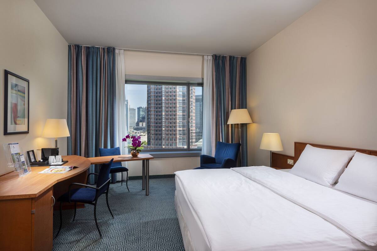 Een hotelkamer met een bed, bureau, stoelen en een raam met gordijnen.