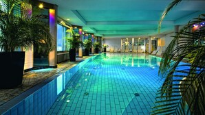Una piscina interior con suelo de baldosas, rodeada de plantas en macetas y sillones de descanso.