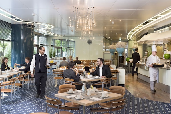 Un comedor moderno con mesas redondas, una estación central de servicio y una cocina a la vista.