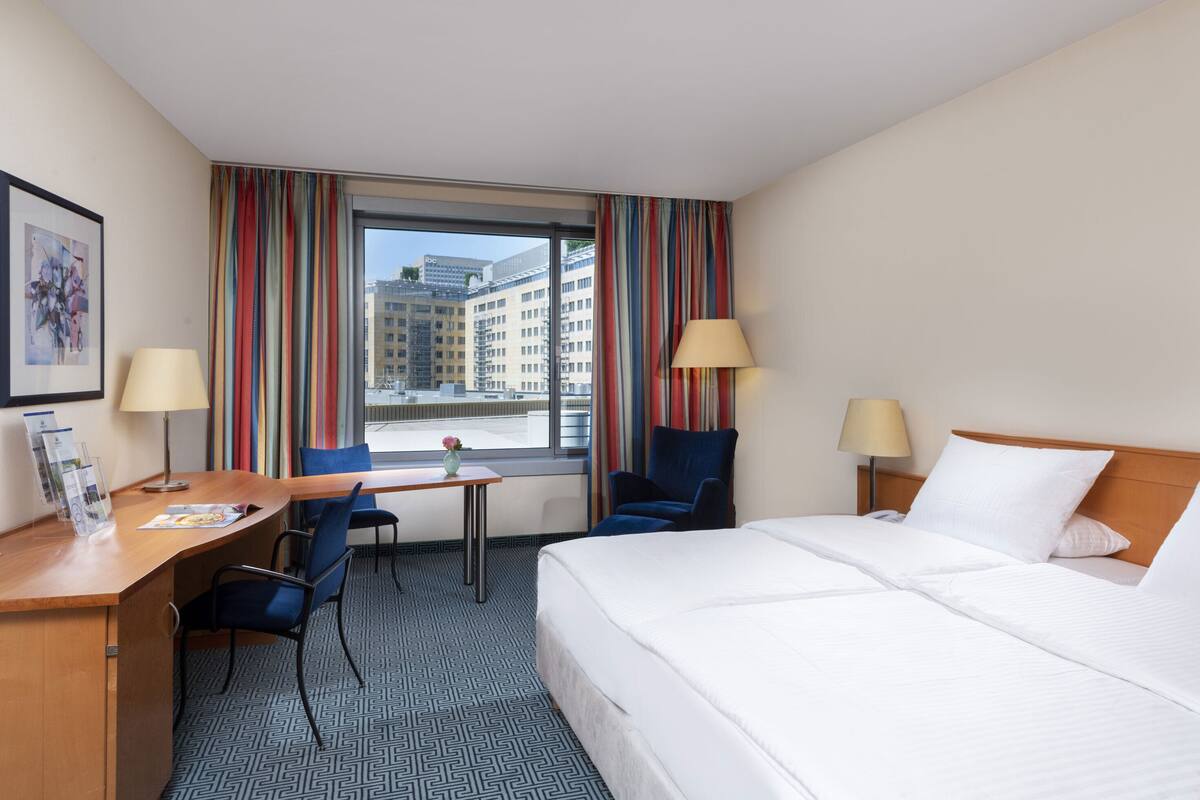 Een hotelkamer met een bed, bureau, stoelen en een raam met gordijnen.
