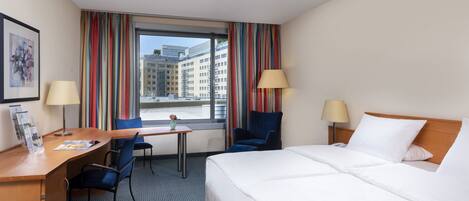 Una habitación de hotel con cama, escritorio, sillas y ventana con cortinas.