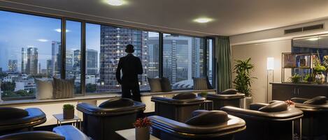 A modern hotel room with a city view, leather seating, a small table with a plant, and a large window.