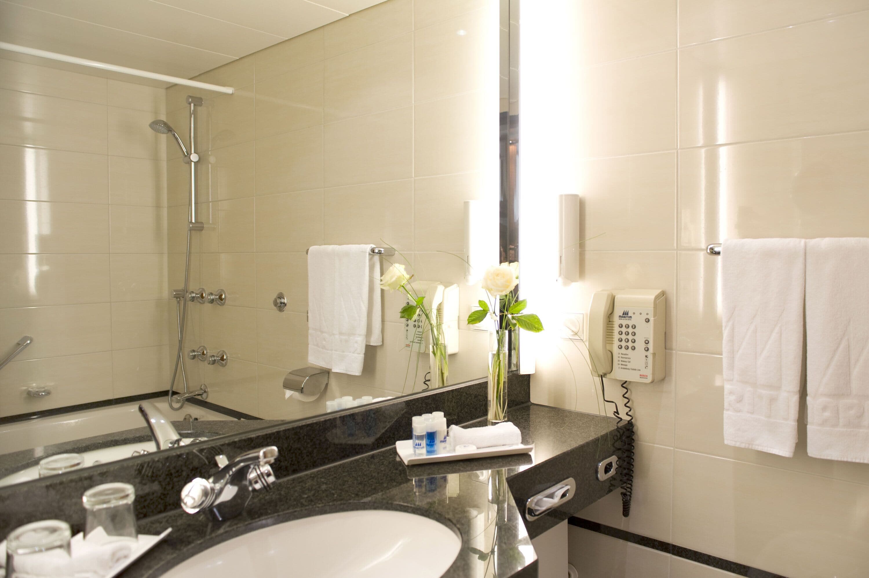Un baño de hotel con un espejo grande, un lavabo, una ducha y un teléfono.