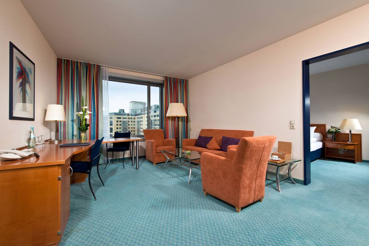 Een hotelkamer met een bureau, twee fauteuils, een bank, een bijzettafeltje en een bed.