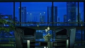 Una habitación moderna con una mesa de vidrio, dos sillas negras y vistas a un paisaje urbano nocturno.