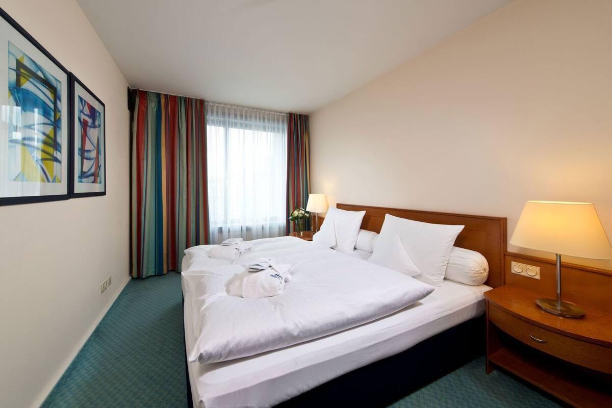 Een hotelkamer met een groot bed, twee nachtkastjes, een lamp en een raam met gordijnen.