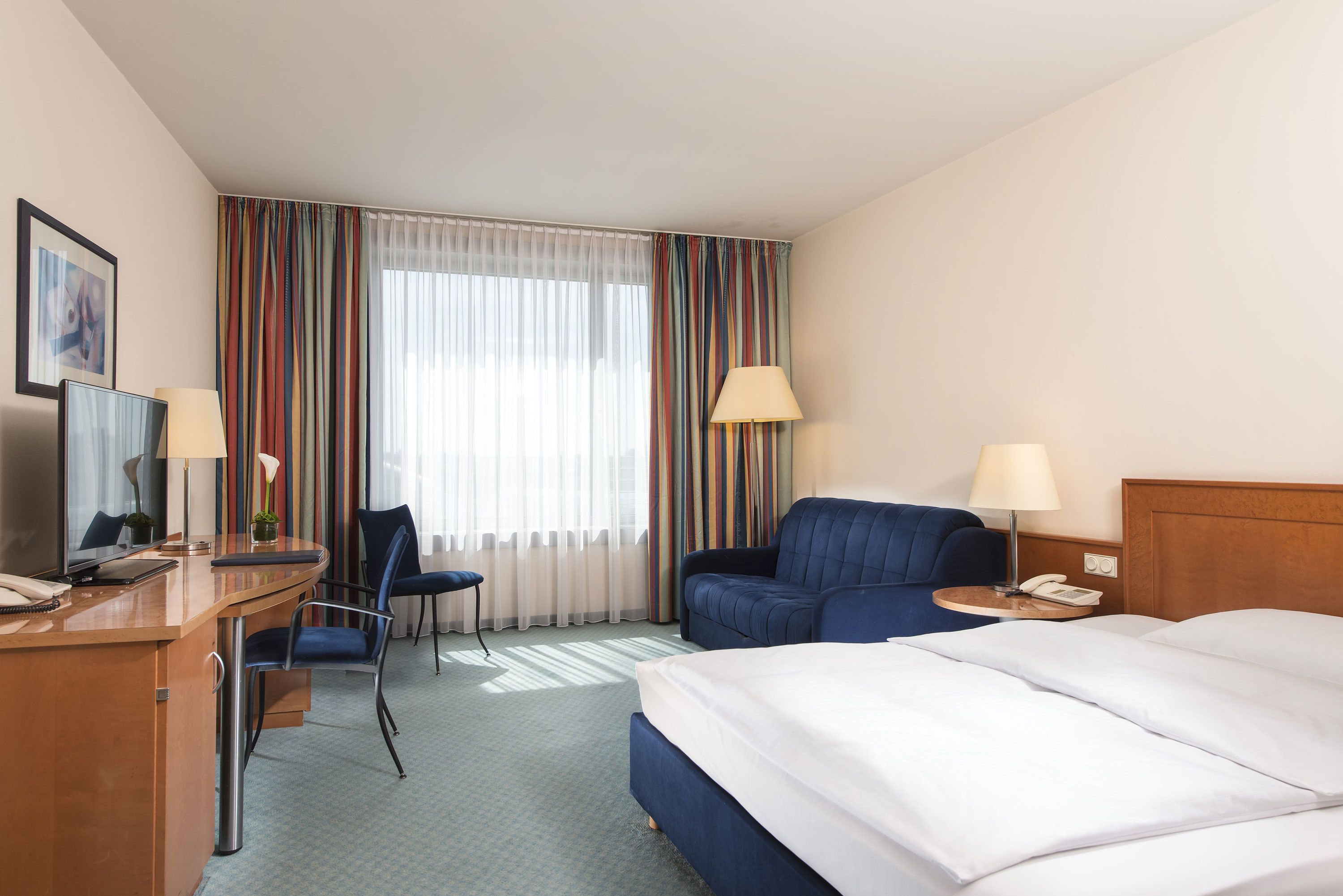 Hotelkamer met een bed, bureau met telefoon, stoel, bank en lamp.