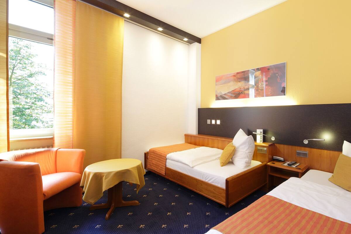 A hotel room with two beds, a sofa, a small table, and a painting on the wall.