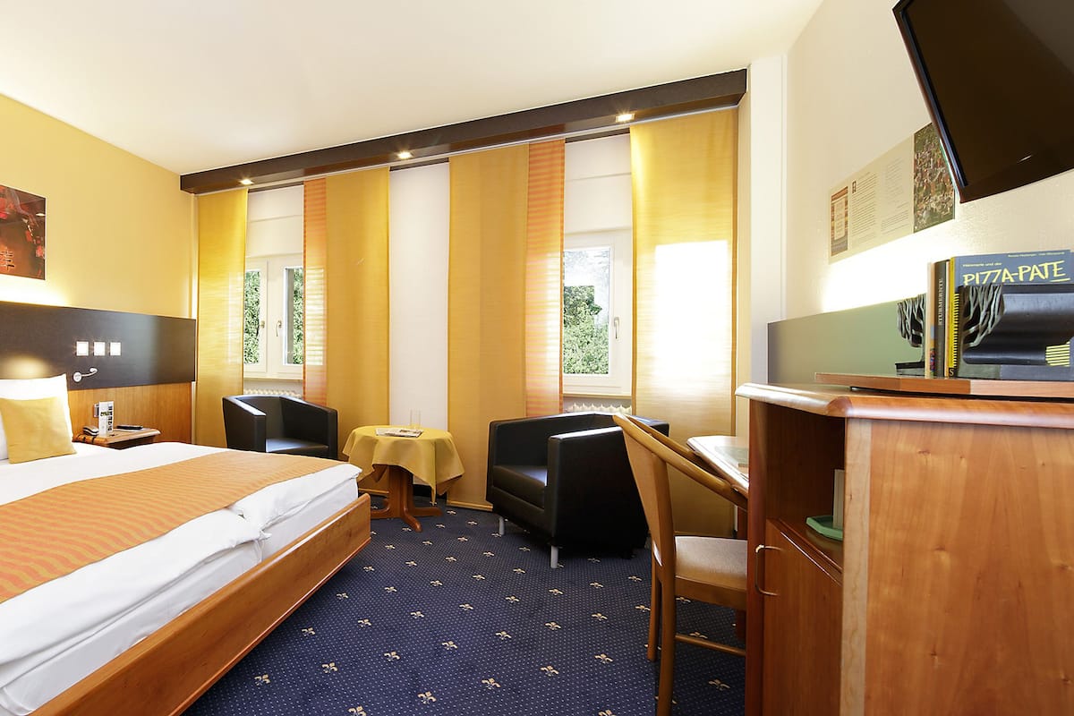 A hotel room with a large bed, a desk, a chair, a small table, and a television.