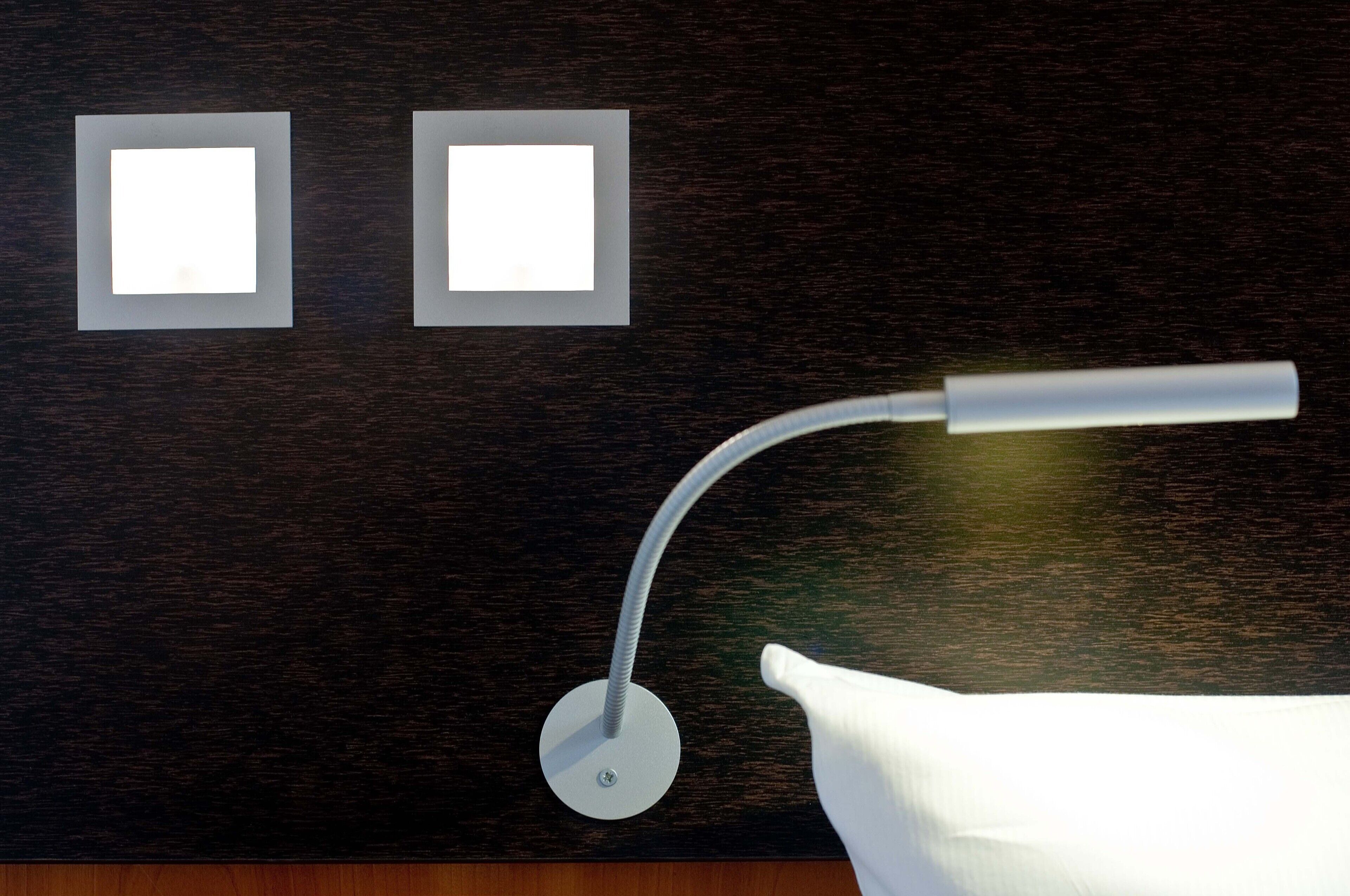 Ein modernes Zimmer mit dunkler Holzvertäfelung, zwei beleuchteten quadratischen Leuchten und einer weißen Lampe mit gebogenem Arm.