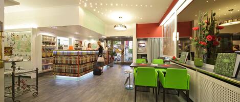 A bookstore with a variety of bookshelves, a counter, and a seating area with green chairs.