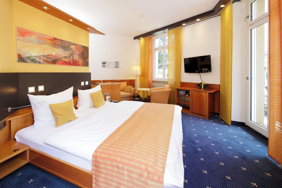 A hotel room with a large bed, a desk, a chair, a television, and a window.