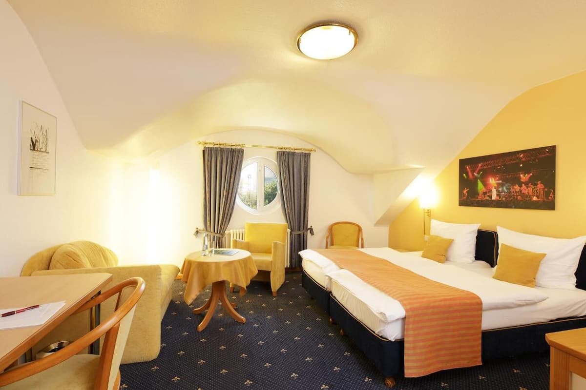 A hotel room with a bed, a desk, a chair, a small table, and a television.