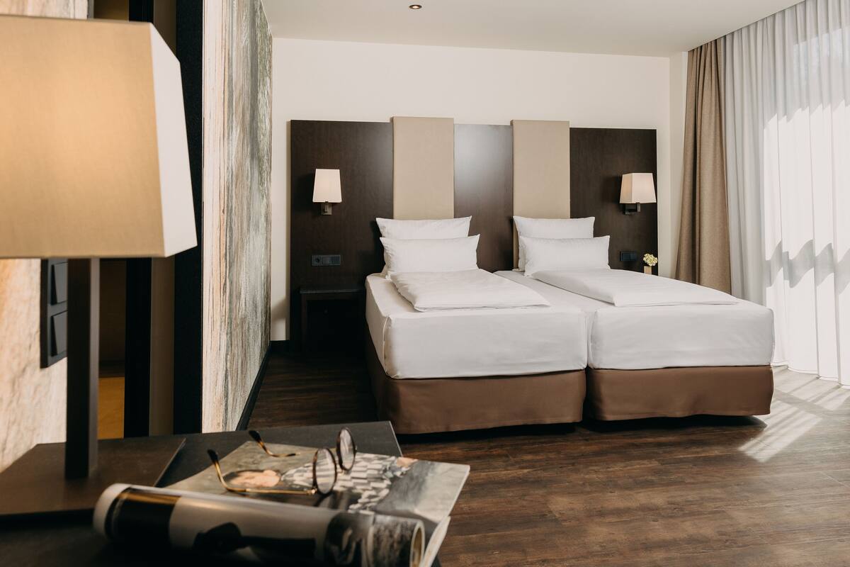 Camera d'albergo con un letto grande, due comodini, una scrivania con una lampada e vista all'esterno.