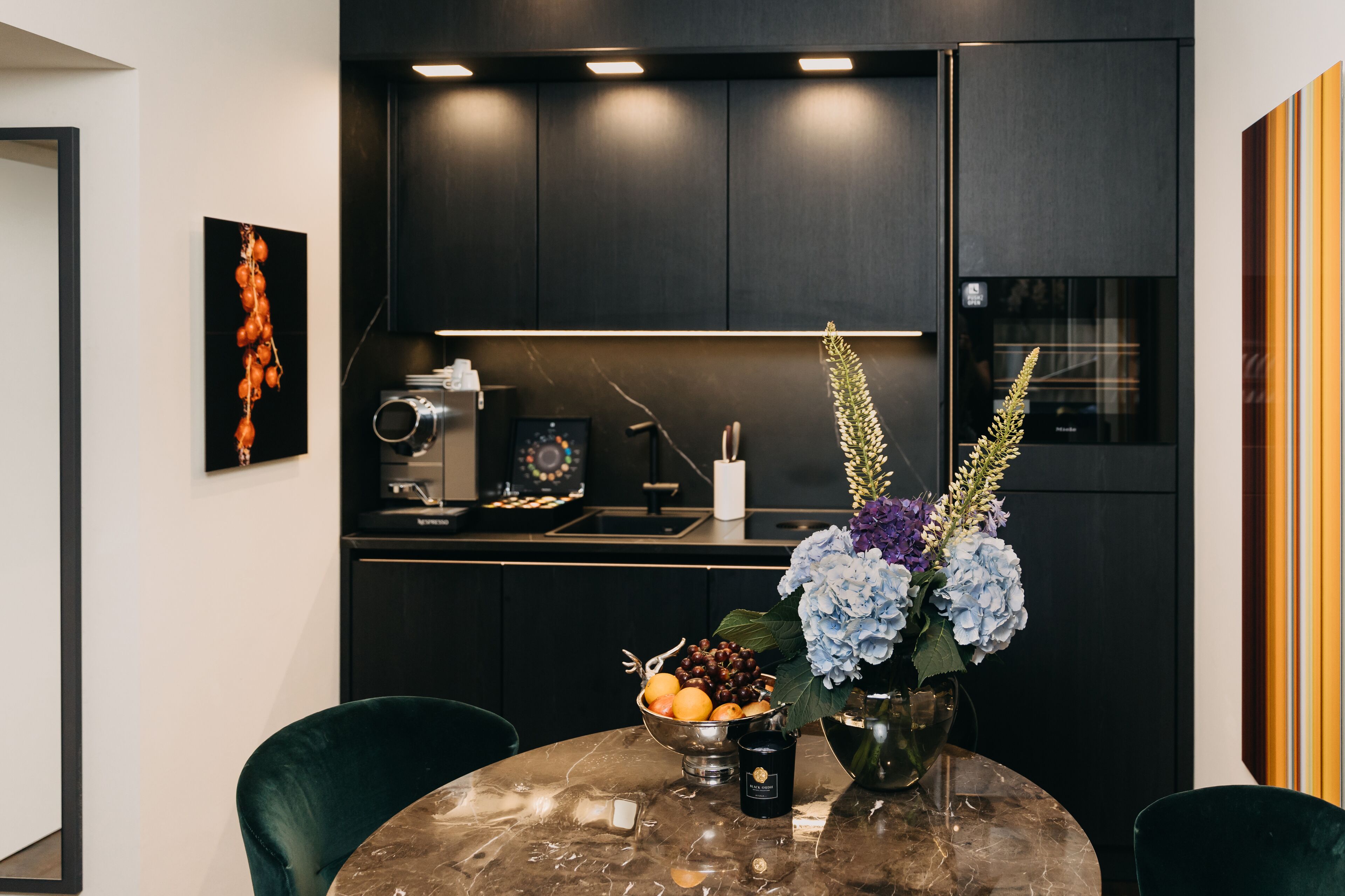 A modern kitchen with dark cabinetry, a marble countertop, and a dining area with a round table and two chairs.