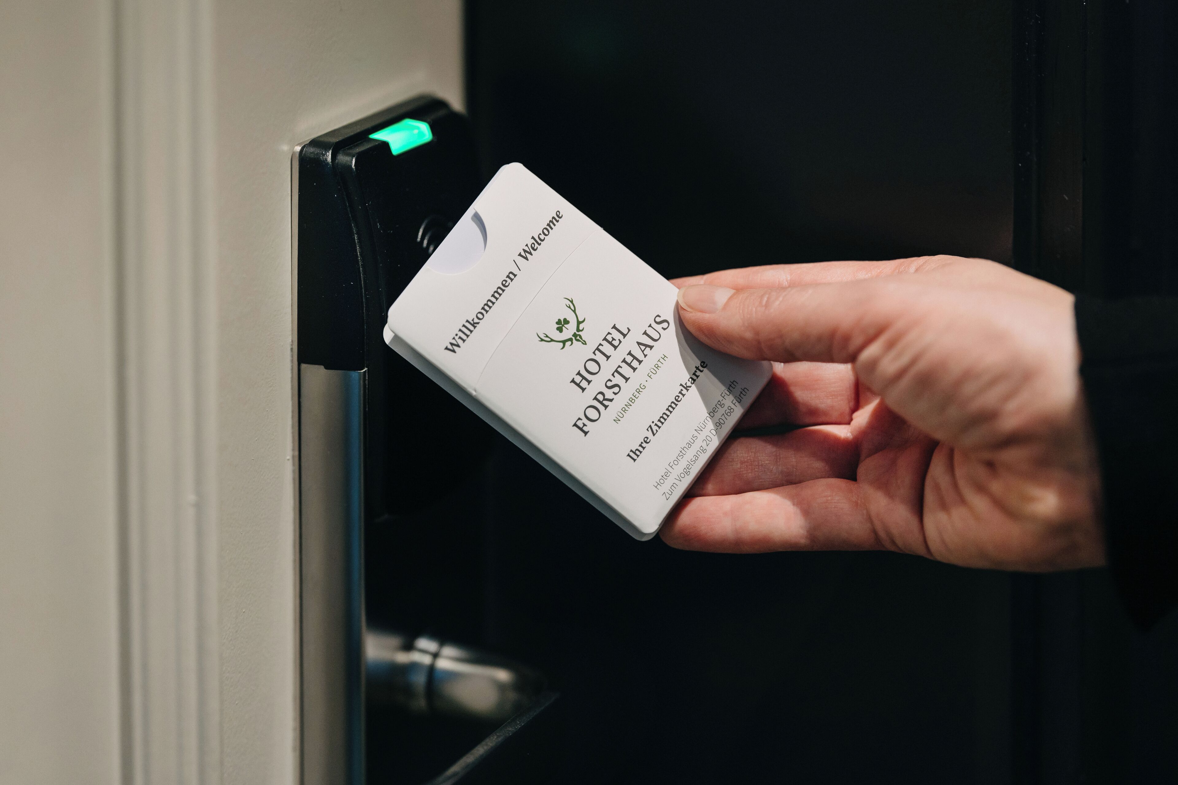 Une main tenant une carte-clé d’hôtel sur laquelle on peut lire le nom « HOTEL FORSTHAUS ».